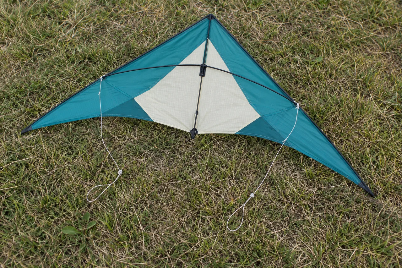 A teal and cream framed kite with pale bridle cords lying on grass